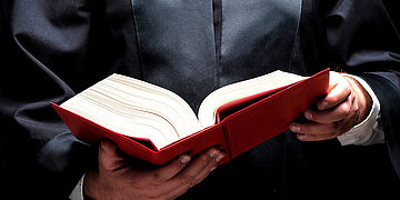 Eine Person in amtlicher Robe hält ein geöffnetes Buch in Händen.