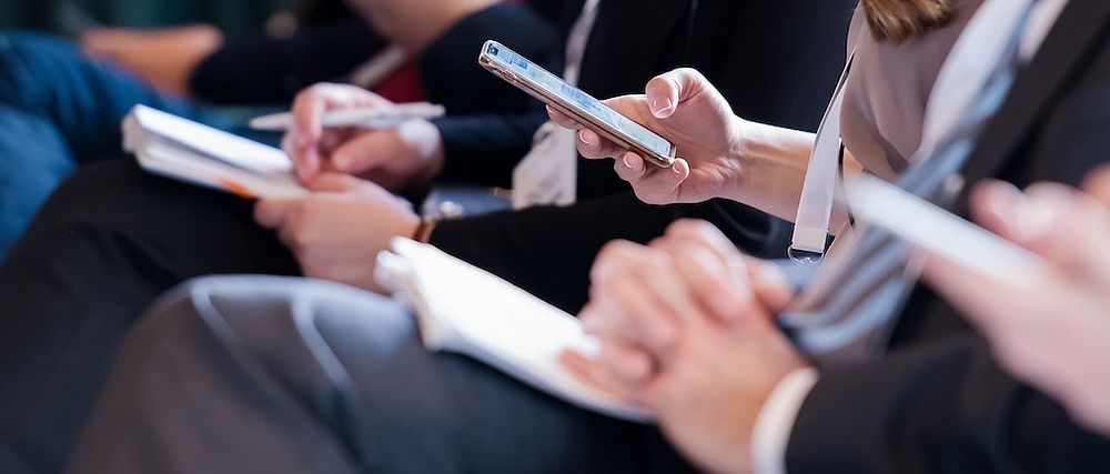 Mehrere Personen schreiben in ihr Notizbuch und tippen in ihr Smartphone.