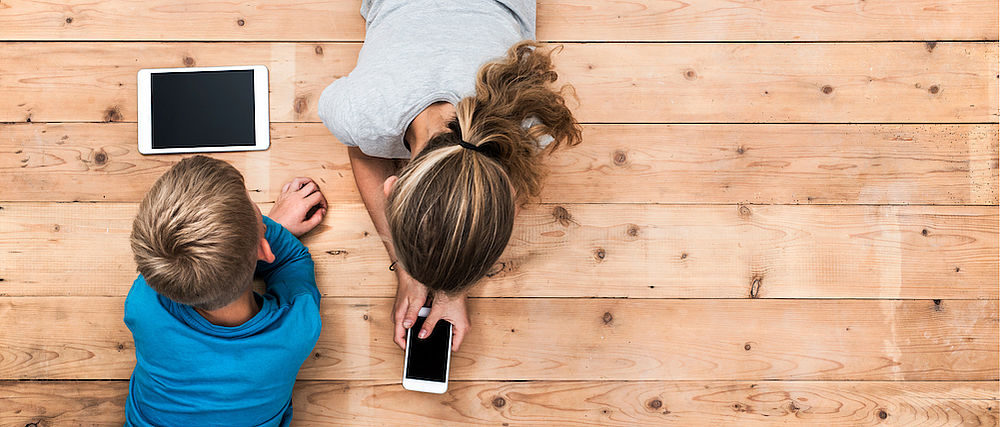 Zwei Kinder liegen auf dem Boden und beschäftigen sich mit ihrem Smartphone und Tablet.