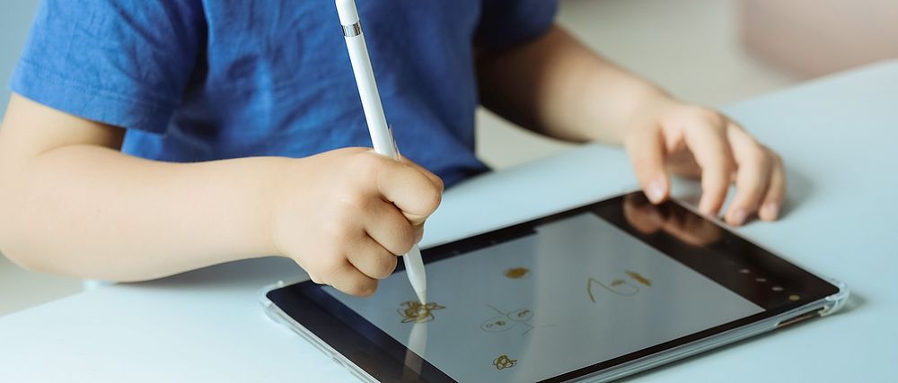 Ein Kind malt mit einem Pen auf einem Tablet.