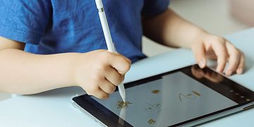 Ein Kind malt mit einem Pen auf einem Tablet.