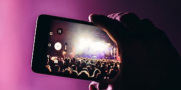 Eine Person filmt ein Konzert mit einem Mobiltelefon.