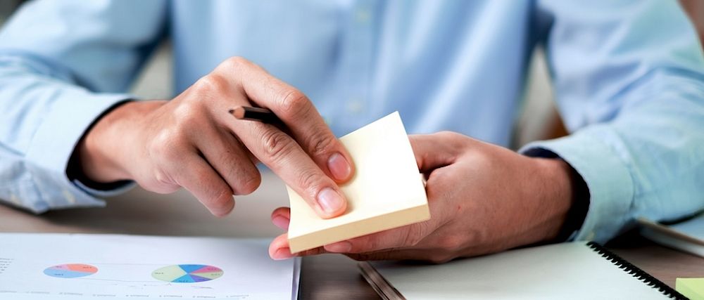 Eine Person zieht einen Klebezettel von einem Post-it-Block.