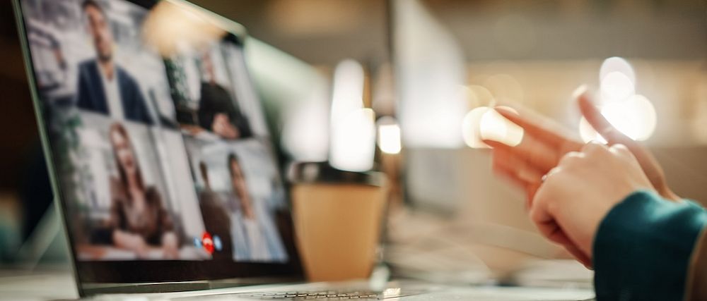 Eine Person sitzt vor einem Notebook, das mehrere Teilnehmer:innen einer Videokonferenz zeigt.