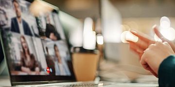 Eine Person sitzt vor einem Notebook, das mehrere Teilnehmer:innen einer Videokonferenz zeigt.